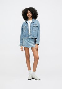 Ελαφρύ τζιν μπουφάν με δύο τσέπες στο στήθος πάνω από ένα λευκό t-shirt, συνδυασμένο με μίνι τζιν φούστα με γραφικό σχέδιο και ξεφτισμένο τελείωμα. Λευκά μποτάκια αστραγάλου.