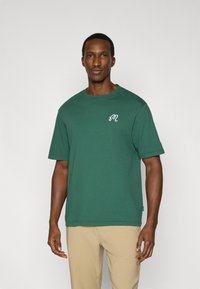 Πράσινο βαμβακερό μπλουζάκι με στρογγυλή λαιμόκοψη και κοντά μανίκια. Διαθέτει μικρό λευκό λογότυπο στο αριστερό στήθος. Λεία υφή. Κανονική εφαρμογή.