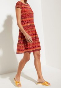 Rotes Kurzarmkleid mit mehrfarbigem Zickzackmuster, A-Linie Schnitt, kombiniert mit gelben Riemchensandalen mit Knotendetail.