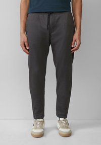 Donkergrijze joggingbroek met een elastische tailleband en trekkoord. Soepele textuur en taps toelopende pasvorm, gedragen met lichtgekleurde sneakers.