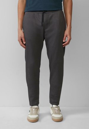 Dark gray jogger pants with an elastic waistband and drawstring. Smooth texture and tapered fit, paired with light-colored sneakers.