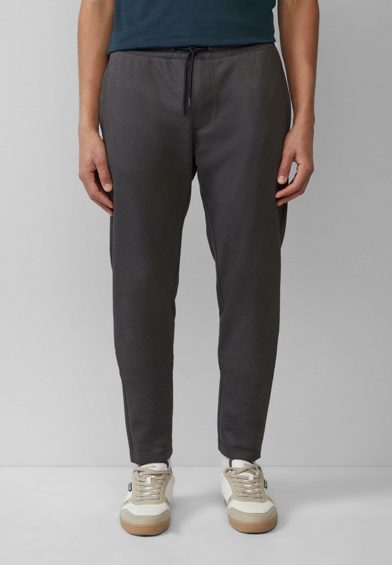 Donkergrijze joggingbroek met een elastische tailleband en trekkoord. Soepele textuur en taps toelopende pasvorm, gedragen met lichtgekleurde sneakers.