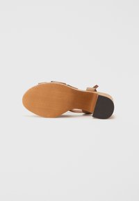 Sandal con tacco in sughero marrone, dotata di una suola liscia color tan testurizzata, con cinturini regolabili e una finitura levigata. Il tacco è a forma conica con una base piatta.