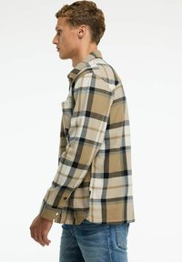 Camisa a cuadros con cuadrados en beige, blanco y negro. Fabricada en una tela suave, con un cierre de botones en la parte delantera y un bolsillo lateral. Manga larga clásica.