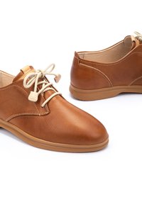 Scarpe in pelle marrone con punta tonda e lacci beige, dotate di suola in gomma color tan e texture morbida con dettagli di cucitura minimi.