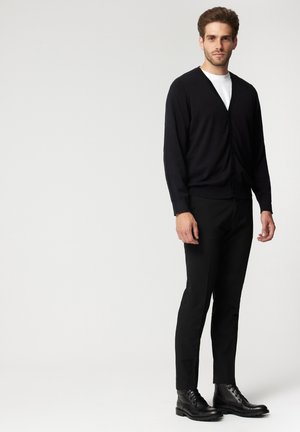 Czarny kardigan z dekoltem w serek i zapięciem na guziki, noszony na białej koszuli. Połączony z czarnymi spodniami i czarnymi sznurowanymi botkami.