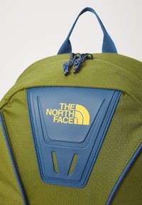Πράσινη τσάντα σακίδιο από ύφασμα με μπλε πλαστική επιφάνεια που φέρει το λογότυπο "The North Face" σε κίτρινο χρώμα, ρυθμιζόμενα μπλε κορδόνια και ενι�σχυμένη λαβή.