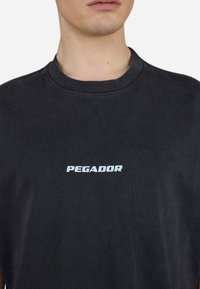 Svart bomull T-skjorte med rund hals, med en hvit "PEGADOR" logo trykket foran. Glatt tekstur, avslappet passform.