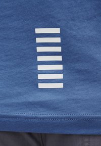 Επτά λευκές οριζόντιες ρίγες, ομοιόμορφα διαχωρισμένες, στο κάτω μέρος μιας μπλε υφασμάτινης ένδυσης με ορατές ραφές.