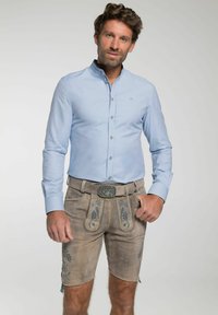 Lichtblauw overhemd met lange mouwen en een button-down kraag, gecombineerd met beige lederhosen met blauwe bloemenborduursels en een decoratieve riemgesp.