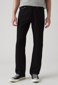 Mustad denim püksid sirge jala disainiga, koos vasevärvi nukkide, klassikalise viie-tasku stiili ja must-valgete tossudega.