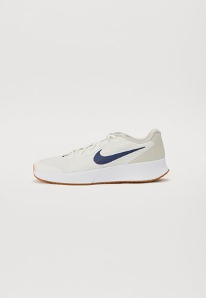 Zapatilla deportiva de Nike en crema claro con swoosh en color marino, parte superior de malla texturizada, suela blanca acolchada y una suela de goma para tracción.