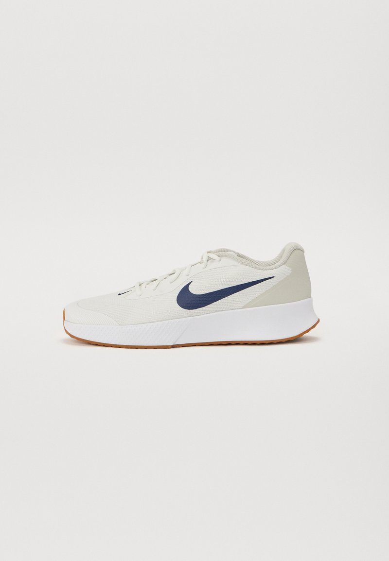 Nike atletska obuća u svijetlo krem boji s tamnoplavim swoosh logotipom, teksturirani mrežasti gornji dio, obloženi bijeli potplat i gumeni potplat za prianjanje.