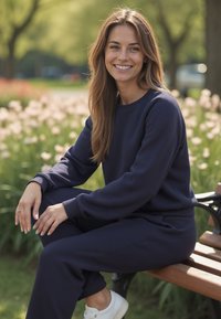 Námořnický modrý, měkký sweatshirt a odpovídající kalhoty s žebrovanými manžetami, nošené s bílými teniskami, sedící na lavičce v parku.
