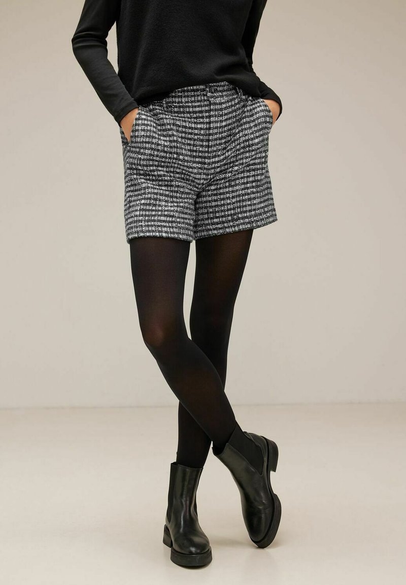 Grå och svart rutiga short med sidofickor, tillsammans med svarta strumpbyxor och ankelboots. Tyget har en texturerad yta.