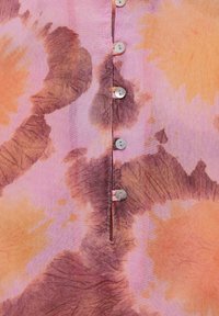 Button-up shirt featuring a tie-dye design in pink, orange, and brown hues. Smooth cotton fabric with circular buttons along the front.