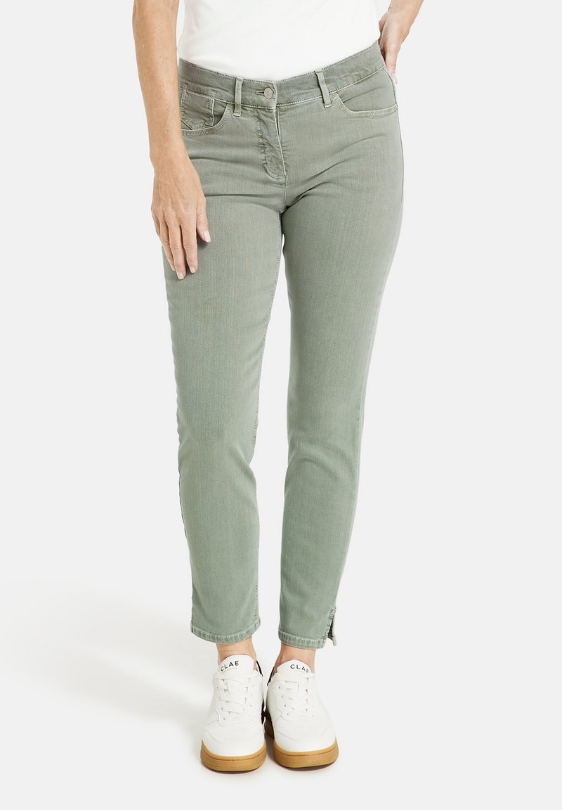 Světlé zelené džíny s fitted designem, s předním zapínáním na knoflík, dvěma bočními kapsami a zipy na kotnících, spárované s bílými teniskami.