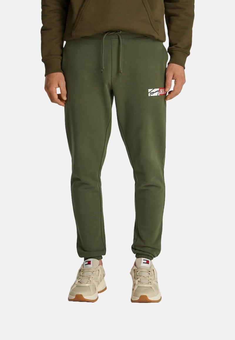Pantalones de chándal verde oliva en una tela suave, con una cintura ajustable, piernas ajustadas y un parche de logotipo impreso en el muslo.