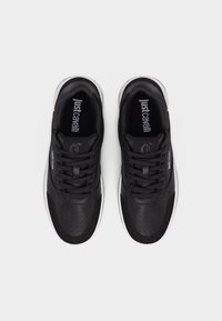 Par črnih superg Just Cavalli z vezalkami, teksturirano usnjeno podrobnostjo in belimi podplati, pogledano od zgoraj na belem ozadju.