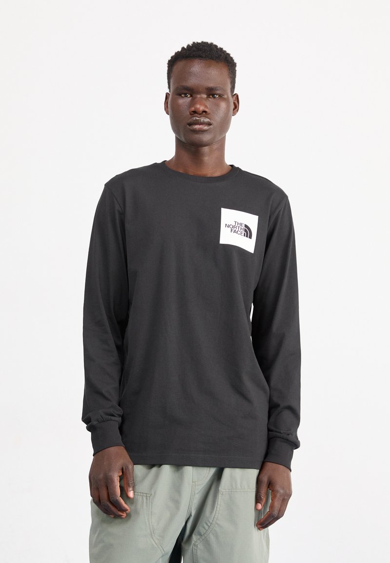 Schwarzes langärmliges T-Shirt aus Baumwolle mit einem weißen Logo auf der Brusttaschenregion. Texturierte Bündchen und eine lockere Passform.