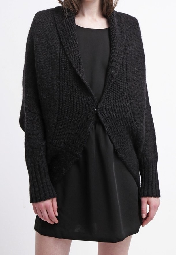 Cardigan noir en tricot avec texture côtelée, manches longues et design ouvert, porté sur une simple robe noire.