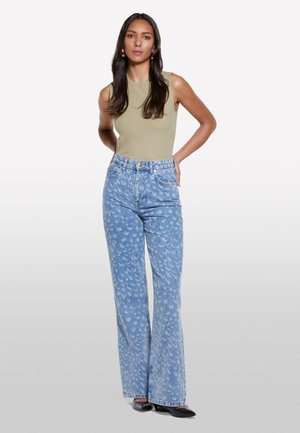 Light olive ribbed tank top paired with high-waisted, light blue jeans featuring a subtle bird pattern. Model wears black flats.