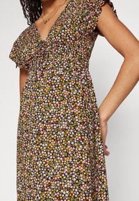 Abito floreale in tessuto nero, con maniche corte a volant e scollatura a V profonda. Il design include piccoli fiori in rosa, arancione e verde.