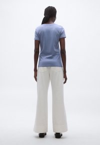 Tricou cu mânecă scurtă de culoare albastru deschis, realizat dintr-un material moale, asortat cu pantaloni albi largi, prevăzuți cu buzunare în spate și tiv curat.