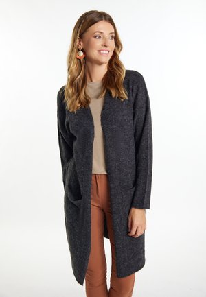 Cardigan lungo grigio scuro realizzato in tessuto testurizzato, con apertura frontale e due tasche frontali, abbinato a un top e pantaloni marrone chiaro.