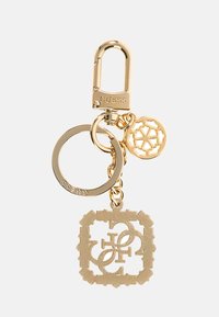 Brelok w odcieniu złota z okrągłym pierścieniem, karabińczykiem i dwoma zawieszkami: dekoracyjną tarczą z logo oraz wzorzystym wisiorkiem z wycięciami.