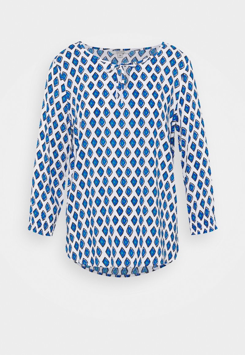 Blouse blanche à manches longues avec un motif losanges bleu et un petit nœud à l'avant au niveau du col.