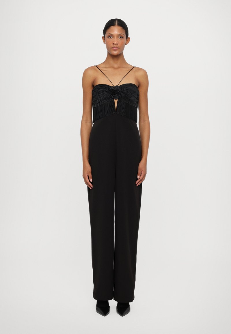 Zwarte jumpsuit met een geplooide lijfje en een centrale strikdetail, dunne bandjes en wijde broekspijpen. Soepele textuur in de hele stof.