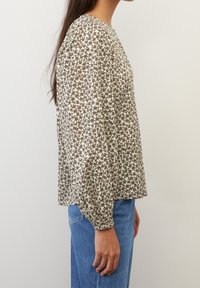 Blusa a maniche lunghe realizzata in tessuto leggero, con un motivo floreale marrone su sfondo crema. Vestibilità comoda con polsini elasticizzati.
