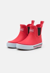 Bottes de cheville en caoutchouc rouge avec des panneaux latéraux élastiques, semelles texturées blanches et accents rayés noir et blanc près de la base.