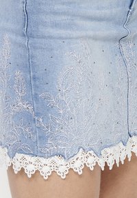 Gonna di jeans di colore azzurro chiaro, con ricami floreali con accenti metallici e orlo in pizzo bianco.