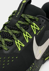 Chaussure de trail Nike noire avec des lacets jaune-vert néon, des œillets assortis, un swoosh blanc et une étiquette Pegasus Trail 5 sur la languette.