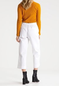 Vita croppade byxor med elastisk midja, kombinerade med en orange ribbat långärmad topp och svarta klackboots vid ankeln.