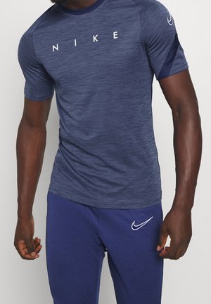 Man wearing blue Nike short-sleeve shirt with white text and matching blue Nike pants with white logo on left thigh.