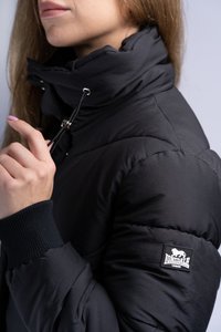 Mustan puffer-jakk on kõrge kraega, nööpide detailiga ja ribakudumistega mansetid. Ühel varrukal on Lonsdale'i logo.