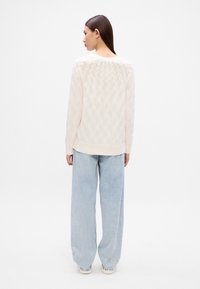 Krémový sveter s káblovým pletením a rebrovanými manžetami, kombinovaný s svetlomodrými nohavicami s širokým strihom. Tkanina má textúrovaný vzor a voľný strih.