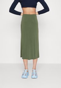 Olivgrön midikjol med elastisk midja, kombinerad med ljusblå chunkysandaler med remdesign och spännen.