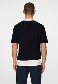 Czarna koszulka z krótkim rękawem z teksturowanym tylnym panelem. Posiada kontrastowy biały kołnierzyk i dół. Wykonana z lekkiego materiału.