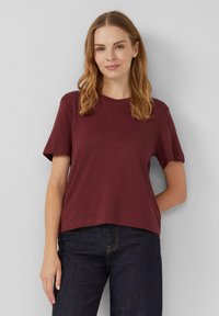 Camiseta de algodón color marrón oscuro con mangas cortas, escote redondo y un corte relajado, combinada con jeans de denim oscuro. Diseño simple y moderno.