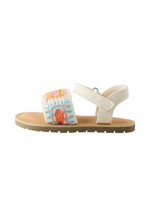 Kindersandale mit offenem Zehenbereich, einer tanfarbenen Sohle, einem beigen Knöchelriemen und einem Häkelriemen vorne mit pastellfarbenen Blumenmustern.