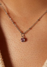 Collier en argent avec un pendentif en pierre précieuse ronde et violette, reposant sur une peau avec une texture visible et des reflets subtils.