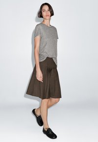 Gray short-sleeve t-shirt paired with a brown pleated skirt, featuring a fitted waistband and black lace-up shoes for a casual look.