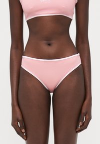 Rozā bikini komplekts ar pieguļošu krūštura augšdaļu un zemu jostasvietu. Mīksta auduma, ar baltu apmalīti, gluda tekstūra, minimāla pārklājuma, un bez rakstiem.