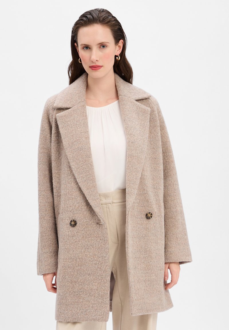 Cappotto in lana beige con un design strutturato, colli oversize e due bottoni scuri, caratterizzato da una texture morbida e una vestibilità rilassata.