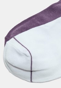 Dettaglio ravvicinato di un calzino con un piede bianco e una parte superiore viola, caratterizzato da una cucitura viola verticale lungo il lato.