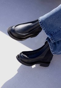 Bottes cheville en cuir noir avec bout arrondi, côtés élastiques et semelles en caoutchouc texturé, associées à un denim bleu.